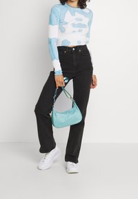 Blå och vit tie-dye långärmad croptop, svarta högmidjade jeans, vita sneakers och en liten turkos handväska med en kort rem.