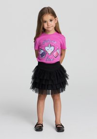 T-shirt rosa con grafica di pozione, abbinato a una gonna a strati in tulle nera. L'outfit presenta un collo rotondo e maniche corte.