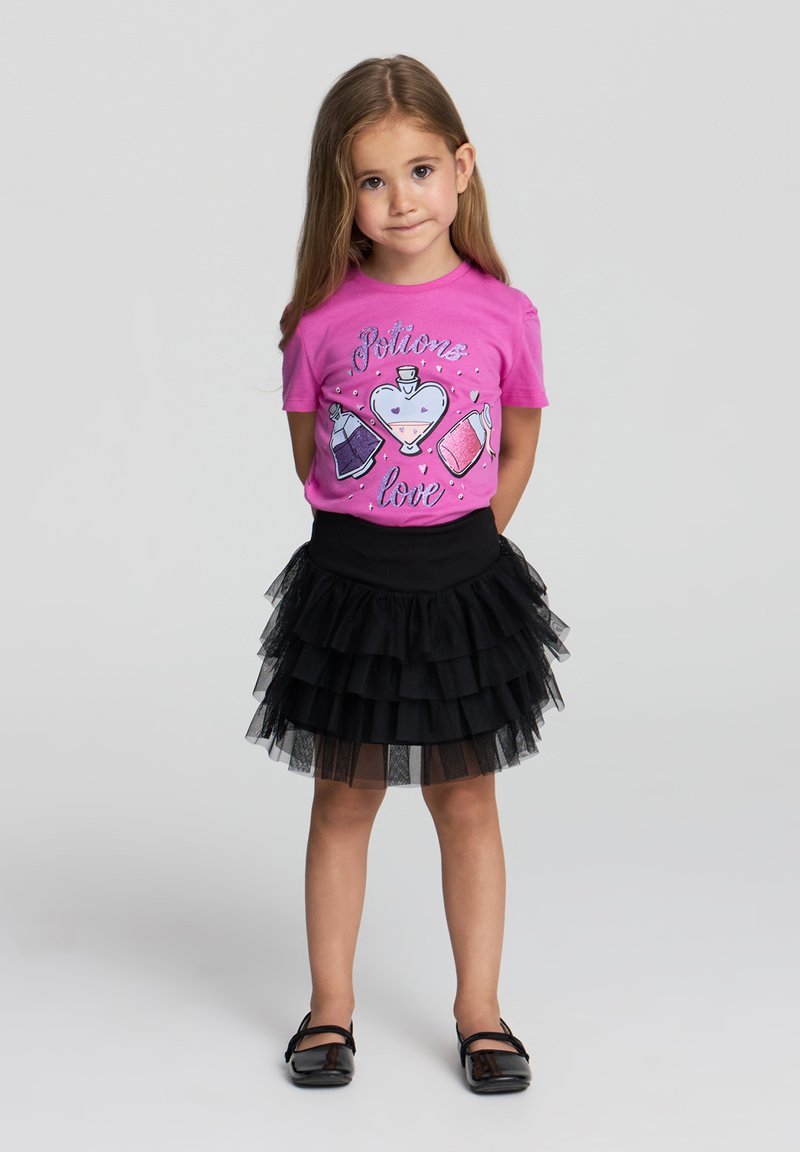 T-shirt rosa con grafica di pozione, abbinato a una gonna a strati in tulle nera. L'outfit presenta un collo rotondo e maniche corte.