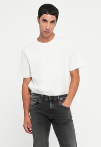 White crew-neck t-shirt with short sleeves, paired with dark gray denim jeans featuring front pockets and a subtle wash texture.