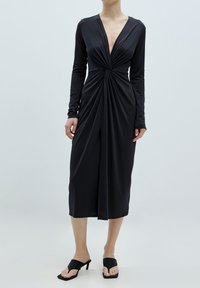 Schwarzes Wickelkleid mit langen Ärmeln und tiefem V-Ausschnitt. Enthält gerafften Stoff an der Taille, knielange Länge, glatte Textur und eine figurbetonte Silhouette.