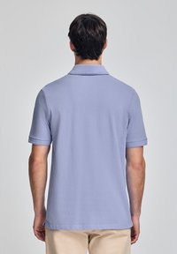 Polo shirt di un leggero colore viola, realizzato in cotone, con colletto classico e maniche corte con dettagli a costine. Texture liscia, design minimale.