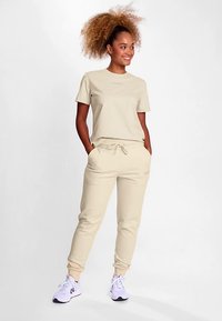 Beżowy bawełniany t-shirt z krótkimi rękawami w połączeniu z dopasowanymi spodenkami dresowymi z elastycznym paskiem i bocznymi kieszeniami. Białe trampki.