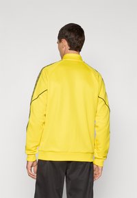 Gul sweatshirt med en mock krave, ribbede ærmer og en sort accent langs siderne. Har et struktureret design på ærmerne.