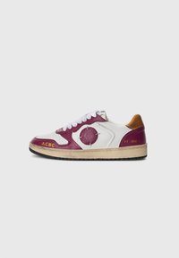 Sneakers con pelle bianca, dettagli in bordeaux, logo rotondo, linguetta beige e suola in gomma nera, con testo di branding giallo.