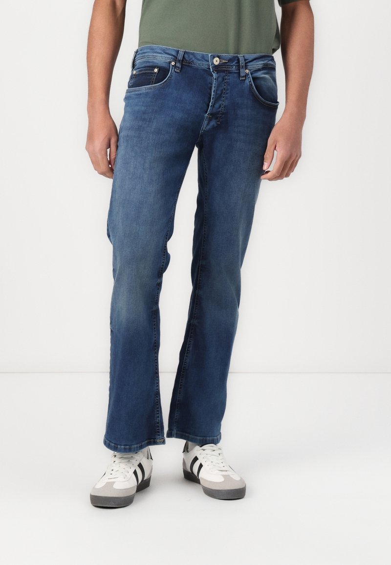 Siniset farkut suorilla lahkeilla, viisi taskua ja kontrastitikkaukset. Varustettu valkoisilla ja harmailla tennareilla.