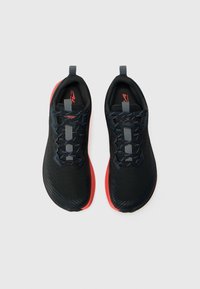 Baskets de course noires avec une surface texturée, lacets gris et une semelle extérieure rouge vif. Dotées d'anses et d'un design profil bas.