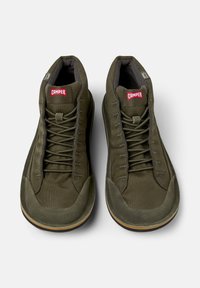 Green high-top sneakers with a textured fabric upper and laces, featuring a red "CAMper" logo on the tongue. Positioned on a white background.