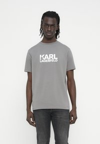 Szara bawełniana koszulka z krótkim rękawem, z białym nadrukiem logo "KARL LAGERFELD" na przodzie. Prosty, okrągły dekolt.