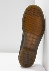 Semelle de chaussure en caoutchouc noir avec un motif texturé, comportant une section de grip translucide de couleur ambre et des détails de marque en relief.