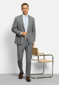 Grau maßgeschneiderter Anzug mit einem hellblauen Hemd. Verfügt über einen Reverskragen, zwei Fronttaschen und braune Schuhe. Schlichtes Design, professionelle Erscheinung.
