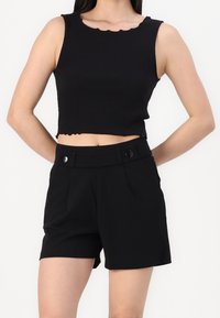 Top croppé noir avec encolure festonnée, associé à un short noir taille haute avec boutons à l'avant et plis.