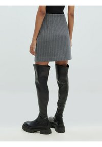 Bottes noires au-dessus du genou avec une semelle épaisse, en cuir lisse. Elles présentent une coupe ajustée, complétées par une jupe gris à rayures au-dessus.