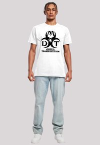 Hvit bomull T-skjorte med svart grafisk design som leser "Department of Magical Transportation," kombinert med lyseblå denim jeans og hvite joggesko.