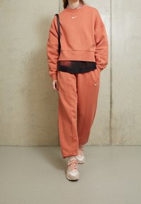 Träningsset bestående av sweatshirt och sweatpants i korallorange, med avslappnad passform, rund hals och subtil logo. Matchas med ljusrosa sportskor.