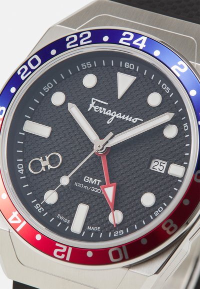 Ferragamo GMT käekell musta tekstureeritud sihverplaadiga, hõbedaste ja punaste detailide, helendavate tundide markeritega ning roostevabast terasest korpusega. Veekindel kuni 100 m sügavuseni.