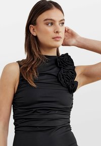 Rochie neagră cu guler înalt, textură plisată și trei trandafiri din material pe umărul stâng. Material neted și elastic.