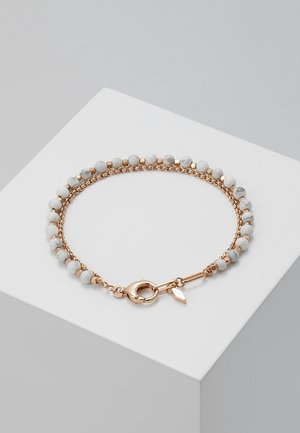 Bracelet chaîne en or avec des perles rondes en marbre blanc et un fermoir homard reposant sur une surface géométrique blanche.