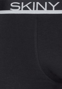 Boxer brief in tessuto nero con cintura marchiata bianca, caratterizzato da una texture liscia e una vestibilità aderente, che enfatizza funzionalità e comfort.