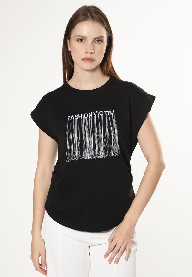 Camisa negra de manga corta con el texto blanco 'FASHION VICTIM' y un diseño con flecos. Material de algodón suave, corte holgado, escote redondo.