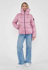 Giacca a vento rosa con colletto alto, chiusura con zip e design trapuntato. Abbinata a jeans a gamba larga azzurri e sneakers bianche.