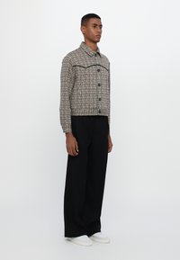 Karirana skraćena jakna s dugim rukavima, kopčanje na dugmad i kontrastni gornji šav. Uparen s širokim crnim hlačama i bijelim tenisicama.