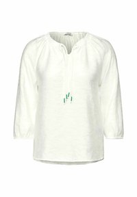 Blusa blanca de lino con escote redondo, detalles fruncidos, mangas tres cuartos y cierre con cordón adornado con acentos verdes.