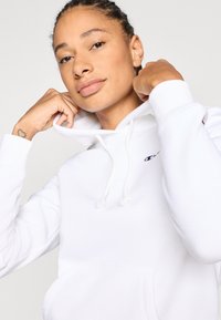 Λευκό φούτερ με κουκούλα και μπροστινή τσέπη, κορδόνι στο καπάκι και μαύρο λογότυπο στο στήθος. Διαθέτει απαλό υφή και ελαστικές μανσέτες.