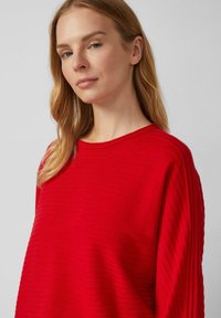 Rotes geripptes Oberteil mit rundem Halsausschnitt und lässiger Passform. Verfügt über einen strukturierten Stoff und überschnittene Schultern. Glatte Textur mit einem dezenten Glanz.