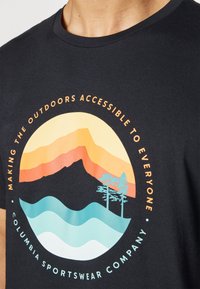 Sort bomulds T-shirt med et cirkulært print af bjerge, træer, bølger og teksten "Gør naturen tilgængelig for alle."