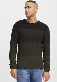 Dark green and black striped knitted sweater with long sleeves and a round neckline, paired with blue denim jeans. Textured fabric with subtle variations.