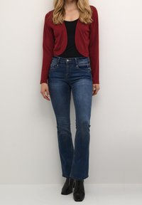 Rode cropped cardigan over een zwarte top, gecombineerd met blauwe flared jeans en zwarte hoge laarzen. Glad textuur, slim fit ontwerp.