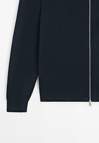 Veste en maille côtelée bleu marine avec manches longues et fermeture éclair argentée sur toute la longueur à l'avant, sur fond blanc.