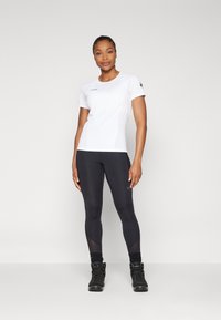 Hvit T-skjorte med korte ermer i atletisk stil sammen med svarte leggings og svarte turstøvler. Har et slankt, moderne design med minimalt med merkevare.