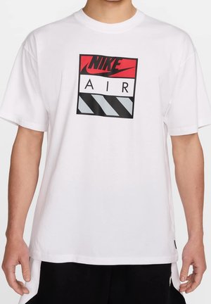 Homme portant un t-shirt blanc Nike Air avec un logo rouge, noir et gris sur la poitrine et un short noir.