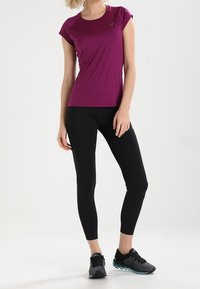 Fitted atletisk tröja i mörkrosa, kort ärm. Svarta leggings med en mjuk textur. Svarta träningsskor med blå detaljer.