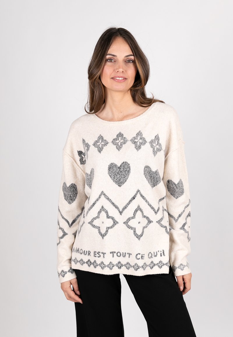 Heller beiger Pullover mit grauen geometrischen Mustern, einschließlich Herzen und Rauten. Hat einen weit geschnittenen Halsausschnitt und lange Ärmel. Weiche Textur.