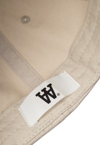 White cotton cap with black logo tag. Interior shows light beige fabric with visible stitching and a round metal eyelet.