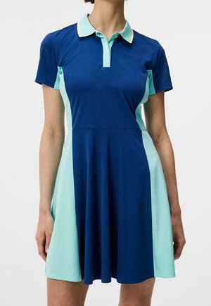 Donna che indossa un vestito polo a maniche corte con pannelli frontali blu navy e laterali acqua, colletto azzurro chiaro e bottoni all'altezza dello scollo.