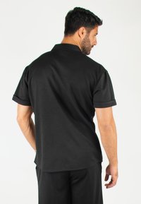 T-shirt polo noir à manches courtes avec des ourlets roulés, présentant un col classique et un ourlet droit, fabriqué à partir d'un tissu lisse et léger.