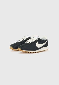 Crne mrežaste i antilop tenisice za trčanje s bijelim swoosh logom, kremastim naglascima, ravnim vezicama i bež gumiranim potplatom s profiliranim gaznim slojem.