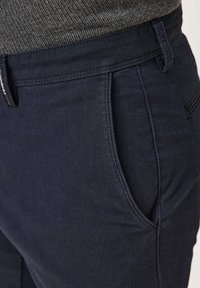 Navyblaue Hosen aus strukturierter Stoffqualität, ausgestattet mit Vorder Taschen und einem taillierten Bund. Das Design ist modern und schnittgerecht zugeschnitten.