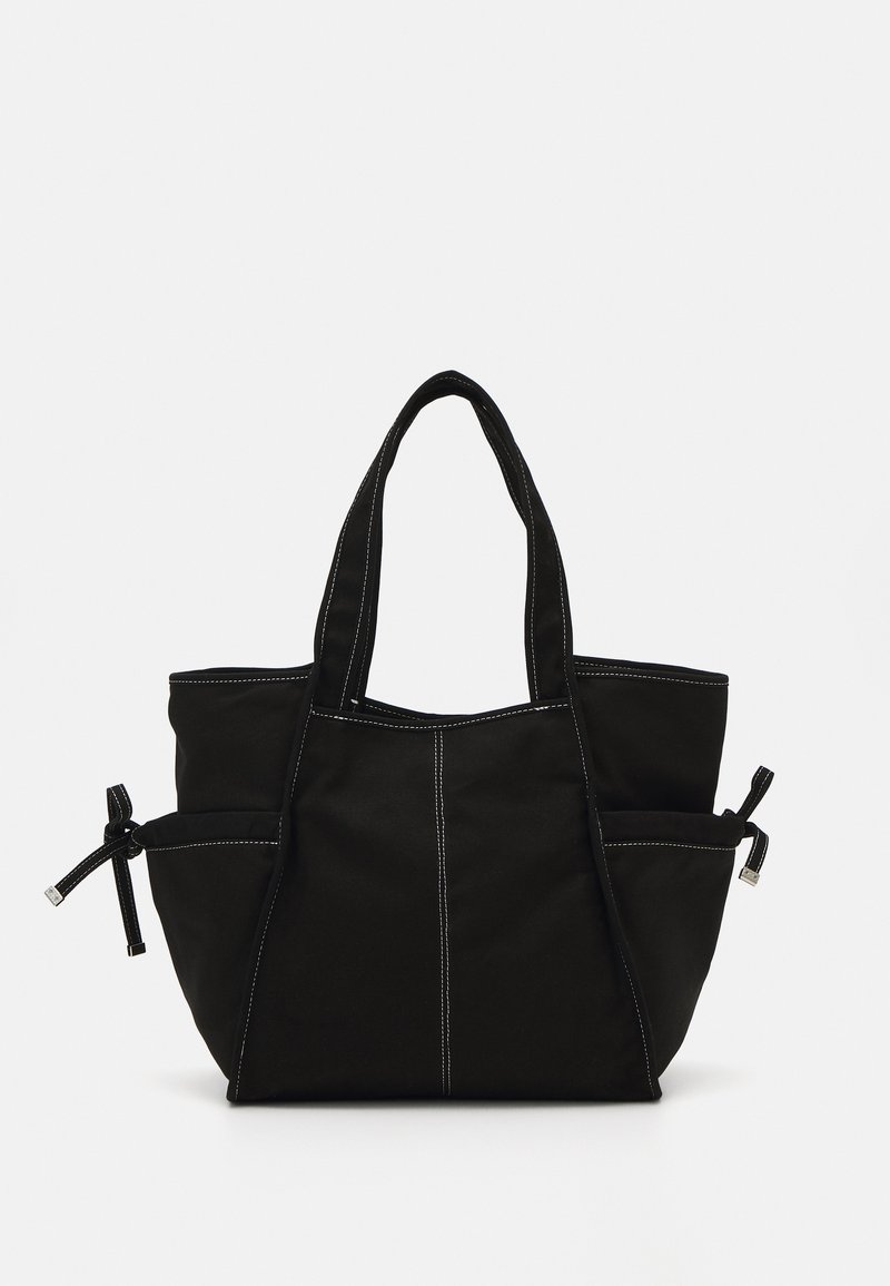 Svart stoff tote bag med hvit søm, to sidelommer med bånd og doble korte håndtak. Myk tekstur med en strukturert form.
