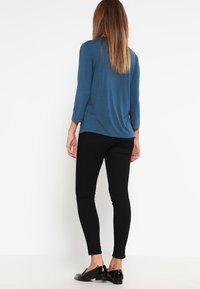 Modrý dlouhý rukáv s volným střihem, v kombinaci s černými skinny kalhotami a černými botami. Hladká látka s jednoduchým designem.