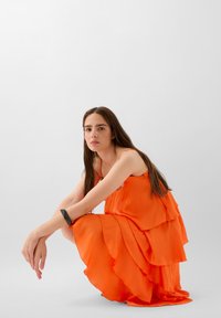 Orange lagdelt kjole med justerbare stropper, lavet af flydende stof. Har et lagdelt design med en blød tekstur og en subtil glans.