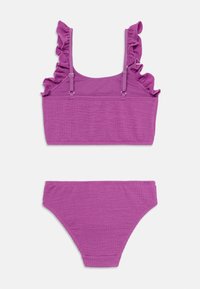 Dvoslojni bikini set od teksturiranog ljubičastog materijala. Gornji dio ima volanaste naramenice i skraćeni dizajn; donji dio ima klasičan kroj.