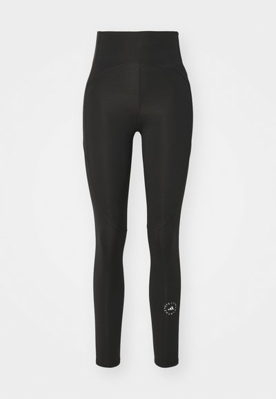Leggings pretos de cintura alta feitos de tecido elástico. Apresentam uma textura suave, ajuste justo e um logótipo circular na parte inferior da perna.