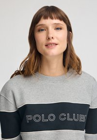 Felpa grigia con una striscia nera che presenta la scritta "POLO CLUB" stampata in bianco. Collo a costine e tessuto strutturato.