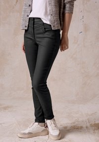 Svarta slim-fit jeans med en slät yta och subtila sömnadsdetaljer, matchade med vita sneakers och en mönstrad cardigan.