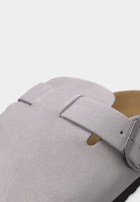 Γκρι ανοιχτό χρώμα γούνινο πάνινο παπούτσι τύπου clog με ασημί ρυθμιζόμενο αγκράφα και καφέ μαξιλαρωμένο πάτο, εμφανίζεται σε κοντινή λεπτομέρεια.